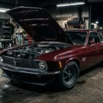 A dramatic, low-angle photograph of a 1970 Ford Mustang Boss 429 in a dimly lit industrial garage setting, the car painted in a deep, rich color with a matte black hood treatment and functional NASA-style hood pins gleaming under harsh overhead workshop lighting. The engine bay is open, revealing the massive 429 cubic inch engine with its distinctive semi-hemispherical cylinder heads and single four-barrel carburetor, the raw mechanical complexity of the Kar Kraft modifications visible in the tight clearances between headers and frame. The Mustang fastback silhouette is bold and purposeful, with a functional front spoiler casting a hard shadow on the concrete floor. The overall mood is serious and technical rather than theatrical, evoking precision engineering and restrained aggression, cinematic depth of field, editorial automotive photography style, high contrast dramatic lighting, photorealistic detail.