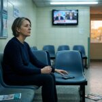 A middle-aged person sitting alone in a sterile hospital waiting room with harsh fluorescent lighting, plastic chairs, and a muted TV on the wall showing blurred news footage. Their hand is frozen mid-reach toward a smartphone resting on the seat beside them, but they have pulled back, choosing instead to sit still with their hands folded in their lap, staring into the middle distance with a contemplative, slightly unsettled expression. The room feels quiet and suspended in time. Through a small window, warm afternoon light filters in, suggesting the world outside moving at a slower, more natural pace. The overall mood is introspective and melancholic, a visual tension between the pull of digital distraction and the rare stillness of an unoccupied mind. Photorealistic editorial style, muted color palette with cool fluorescent blues contrasted against warm amber tones from the window, shallow depth of field.
